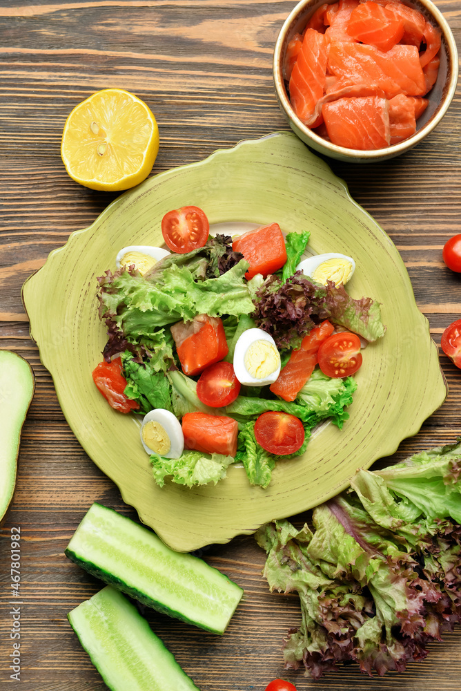 Tasty salad with salmon and fresh vegetables in plate on wooden background