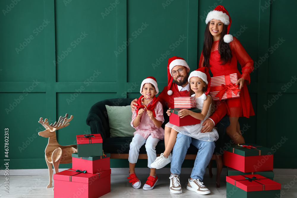 Happy family in Santa hats with Christmas gifts near green wall