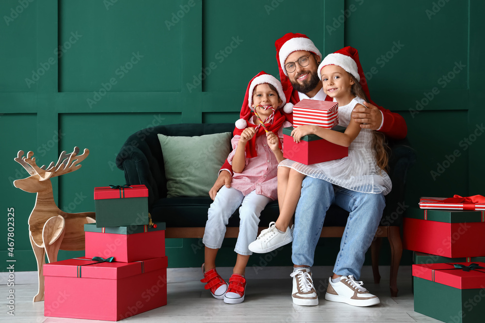 Happy family in Santa hats with Christmas gifts near green wall