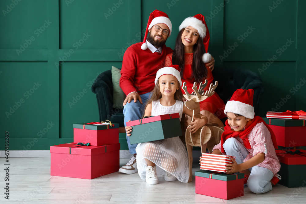 Happy family in Santa hats with Christmas gifts near green wall