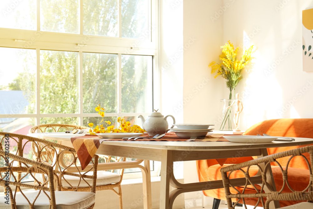 Wooden table with dishes and flowers in light dining room