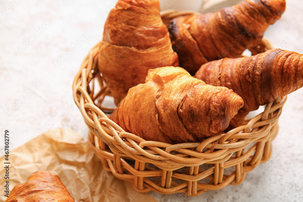 Wicker basket with delicious croissants on light background, closeup