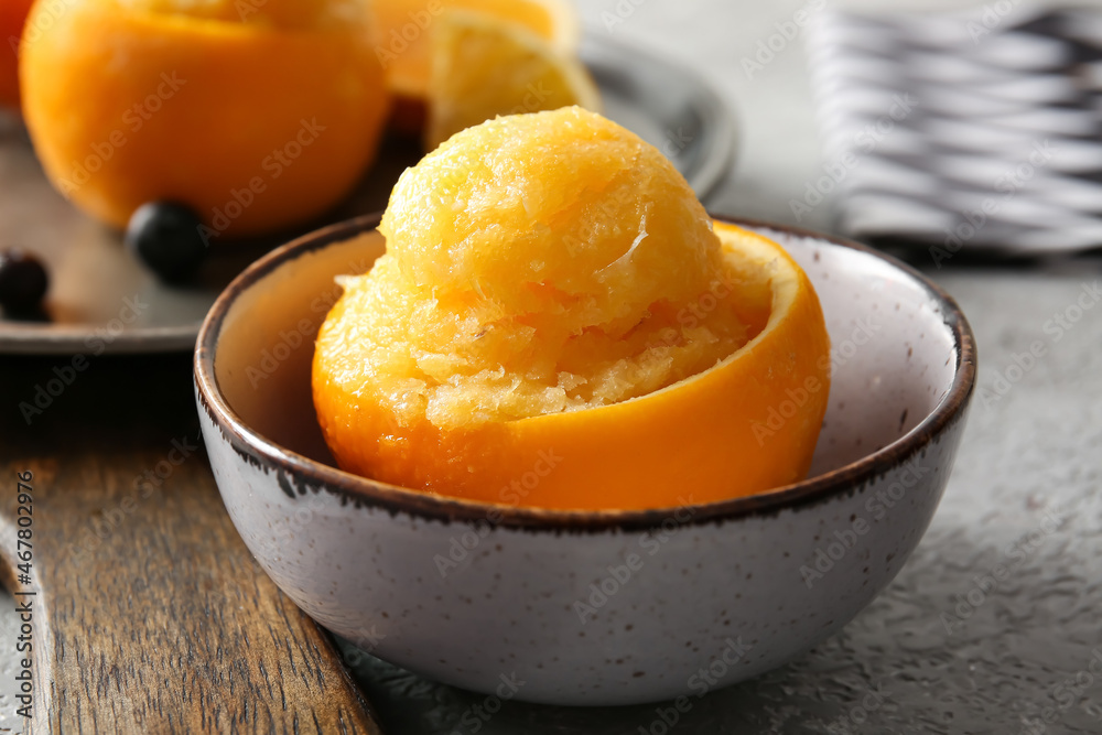 Bowl with tasty ice creams in orange peels on grey background