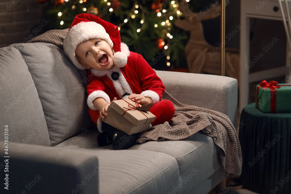 Cute little boy in Santa costume and with gift at home on Christmas eve