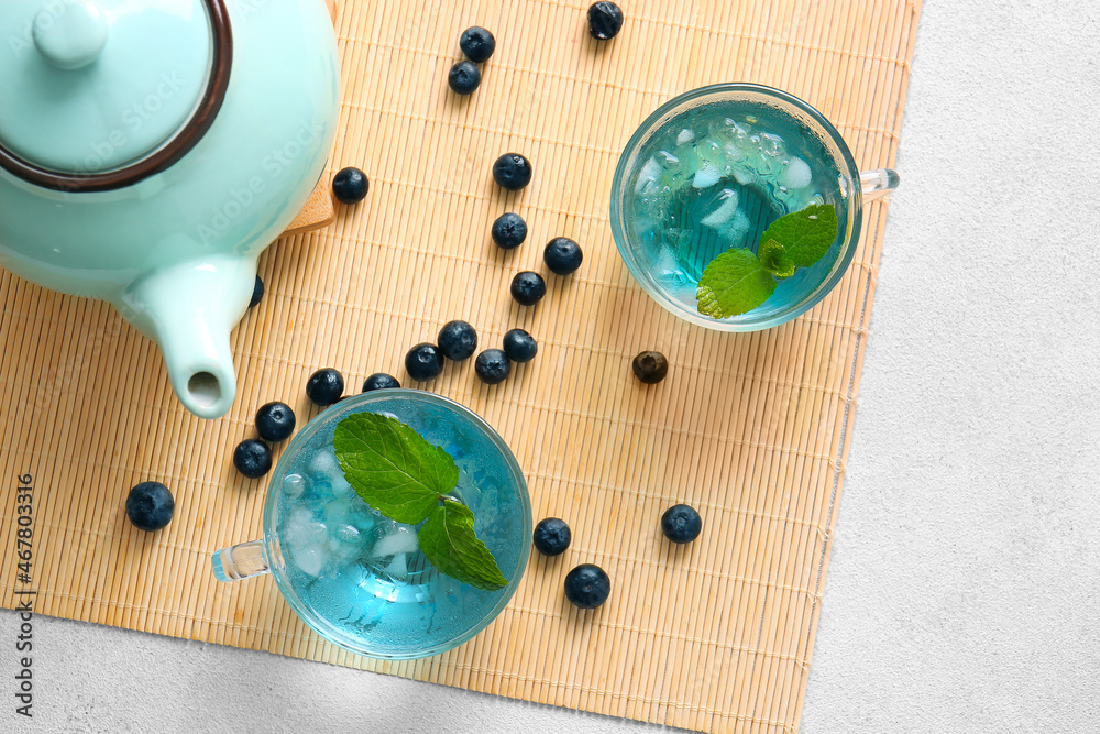 Glass cups of iced blue tea and blueberry on light background