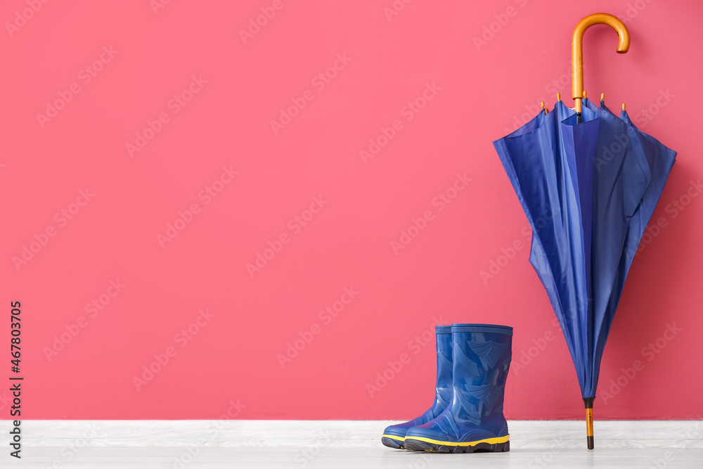 Pair of rubber boots and umbrella on floor against color wall