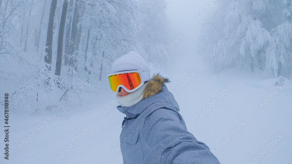 自拍：戴着橙色护目镜的女单板滑雪运动员沿着滑雪场的斜坡骑行。