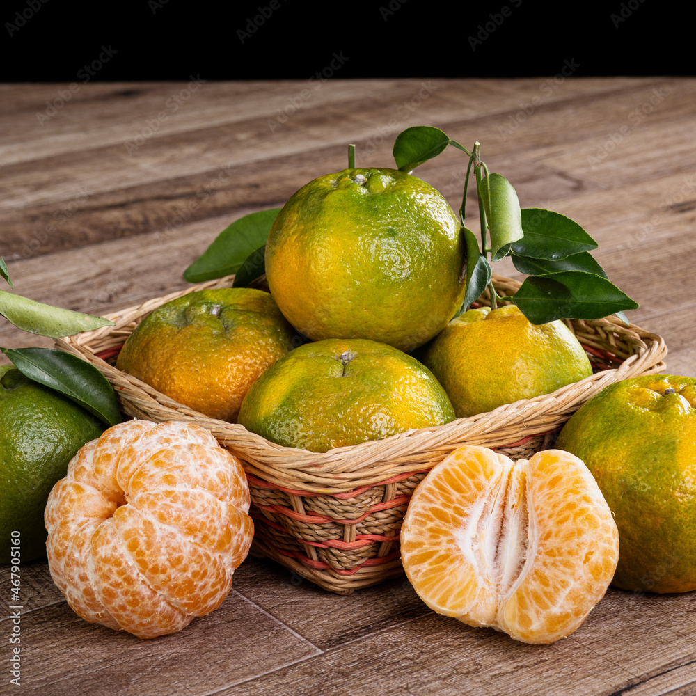 Fresh green tangerine on dark wooden table with black background.