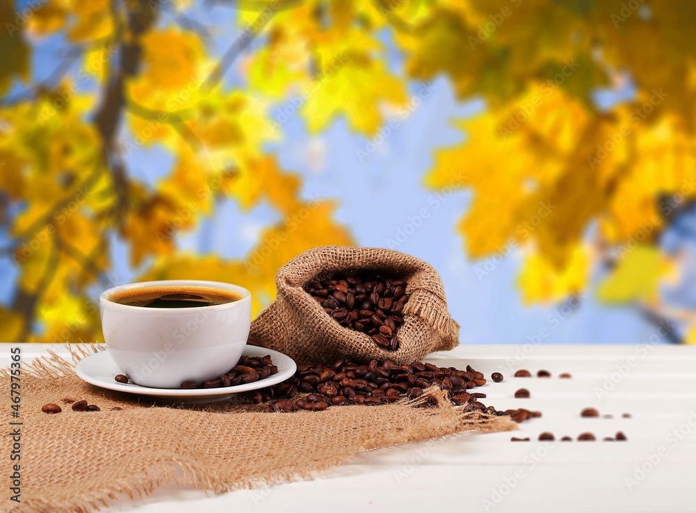 Hot coffee in a white coffee cup and many beans placed around