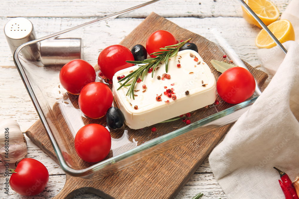 Baking dish with feta cheese, olives and tomatoes on light wooden background