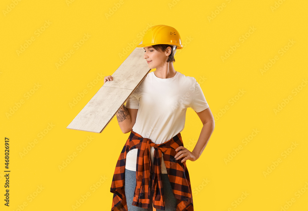 Female construction worker in hardhat with wooden plank on yellow background