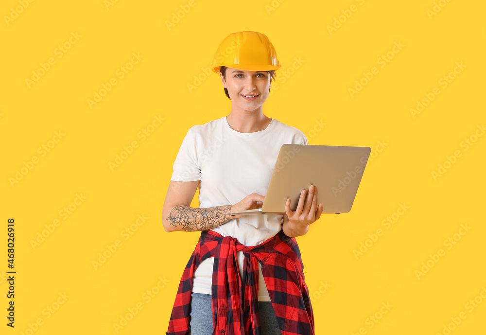 Female construction worker in hardhat using laptop on yellow background