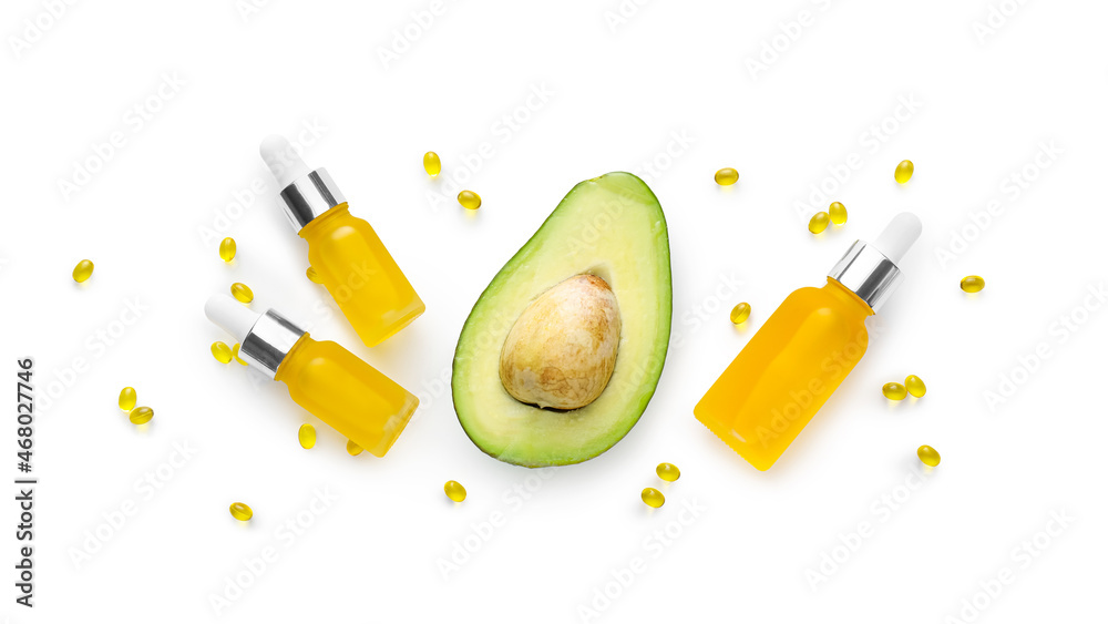 Bottles of essential oil, capsules and avocado on white background