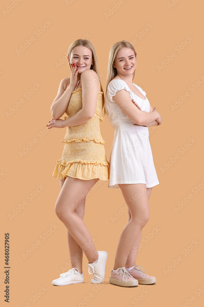 Young blonde twin sisters on beige background