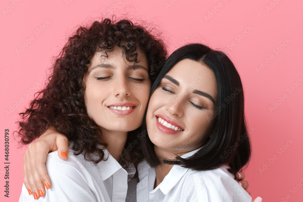 Happy sisters with closed eyes hugging on color background, closeup