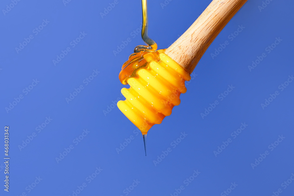 Pouring of sweet honey from dipper on blue background, closeup