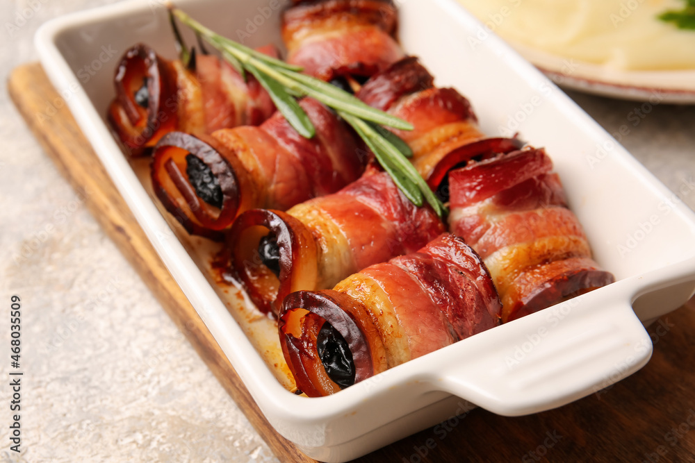 Baking dish with tasty prunes baked in crispy bacon on table, closeup