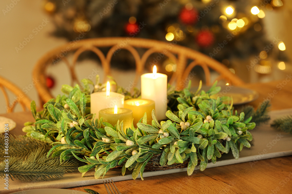 Beautiful mistletoe wreath with candles on table served for Christmas dinner