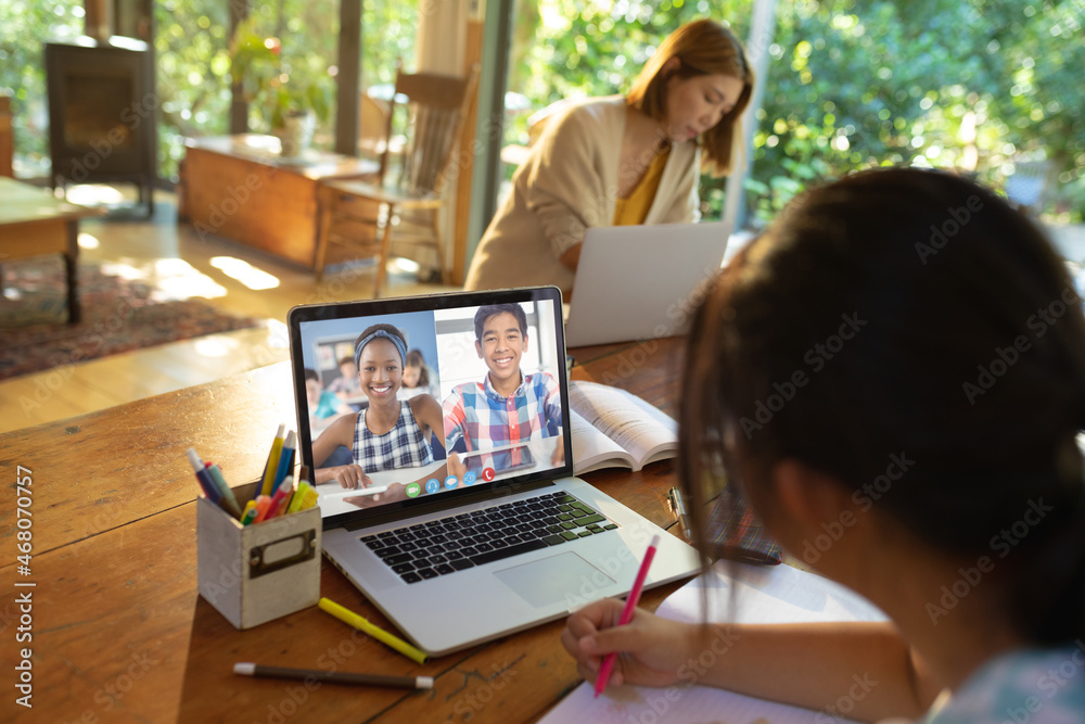 Asian girl using laptop for video call, with smiling diverse high school pupils on screen