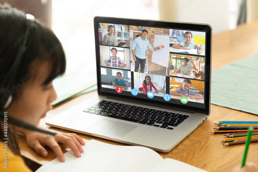 Asian girl using laptop for video call, with smiling diverse elementary school pupils on screen