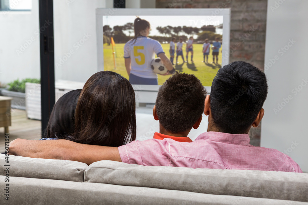 Rear view of family sitting at home together watching football match on tv