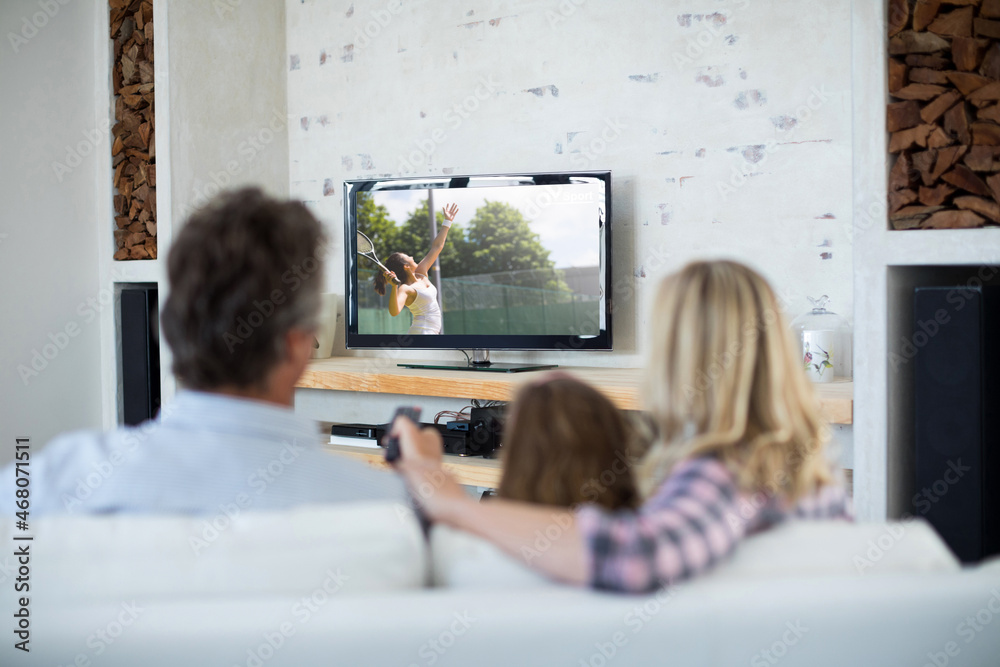 Rear view of family sitting at home together watching tennis match on tv