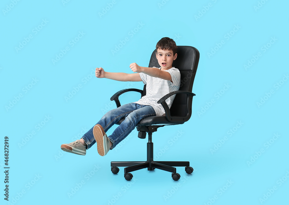 Little boy with imaginary steering wheel sitting in chair on color background