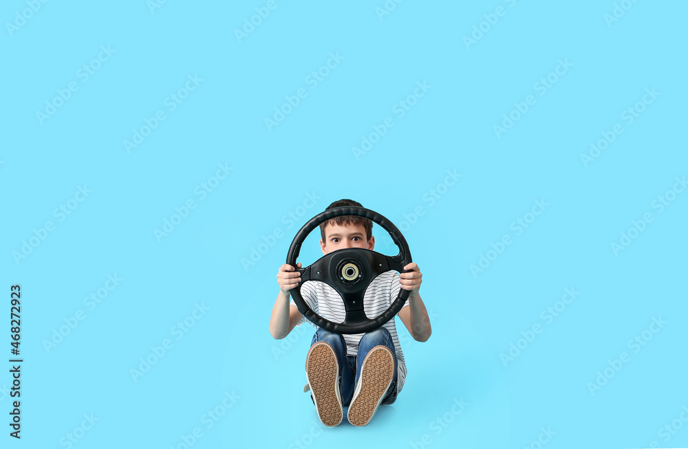 Cute little boy with steering wheel on color background