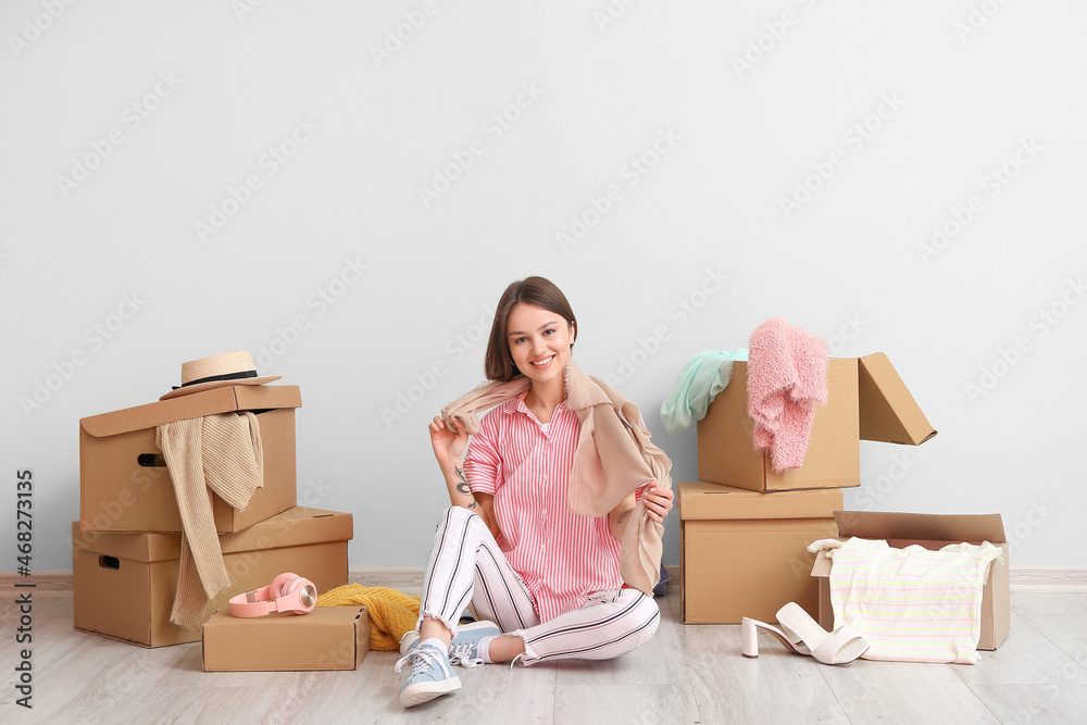 Young woman with clothes and wardrobe boxes near light wall