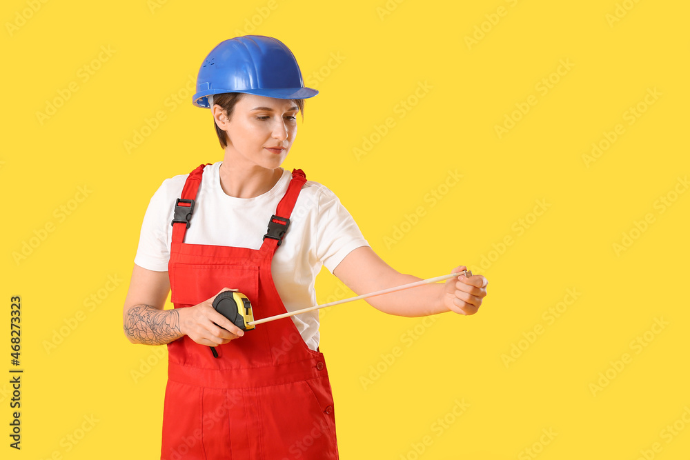 Female construction worker in hardhat with measuring tape on yellow background