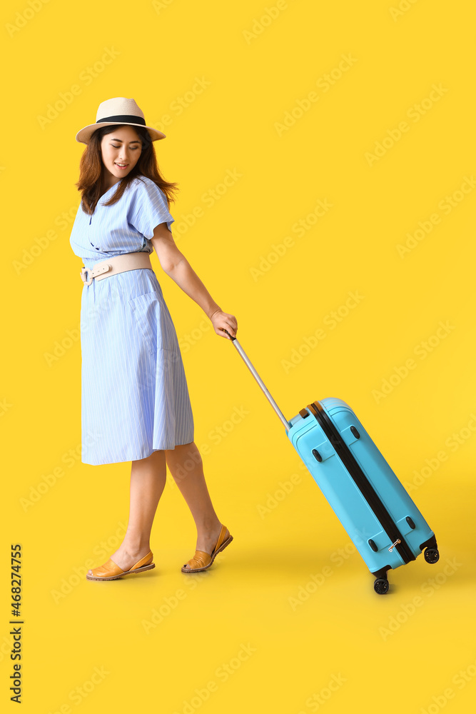 Young woman with suitcase on color background