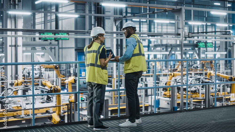 Male Specialist and Female Car Factory Engineer in High Visibility Vests Using Laptop Computer. Auto