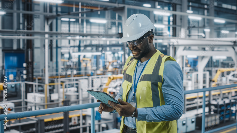 African American Car Factory Engineer in High Visibility Vest Using Tablet Computer. Automotive Indu