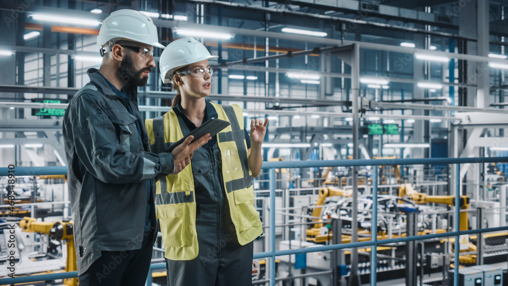 Male Specialist and Female Car Factory Engineer in High Visibility Vests Using Tablet Computer. Auto