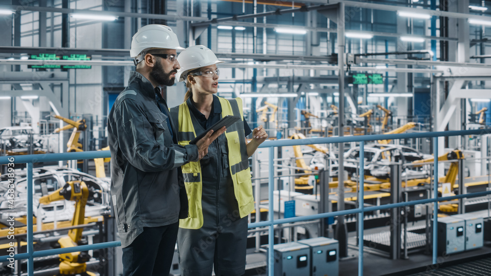 Male Specialist and Female Car Factory Engineer in High Visibility Vests Using Tablet Computer. Auto