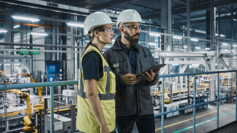 Male Specialist and Female Car Factory Engineer in High Visibility Vests Using Tablet Computer. Auto