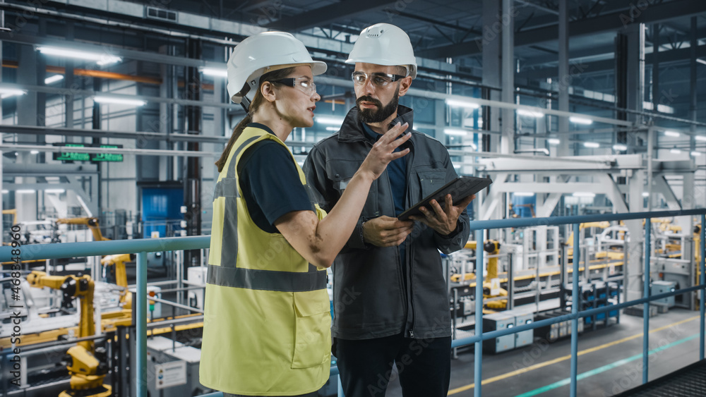 Male Specialist and Female Car Factory Engineer in High Visibility Vests Using Tablet Computer. Auto