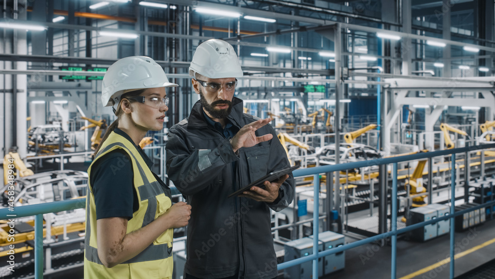 Male Specialist and Female Car Factory Engineer in High Visibility Vests Using Tablet Computer. Auto