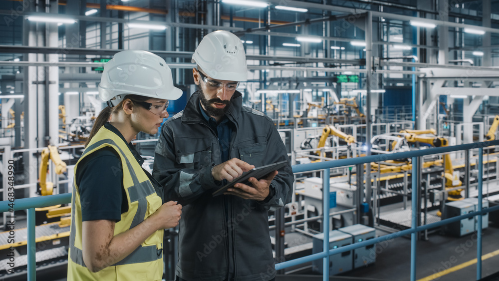 Male Specialist and Female Car Factory Engineer in High Visibility Vests Using Tablet Computer. Auto