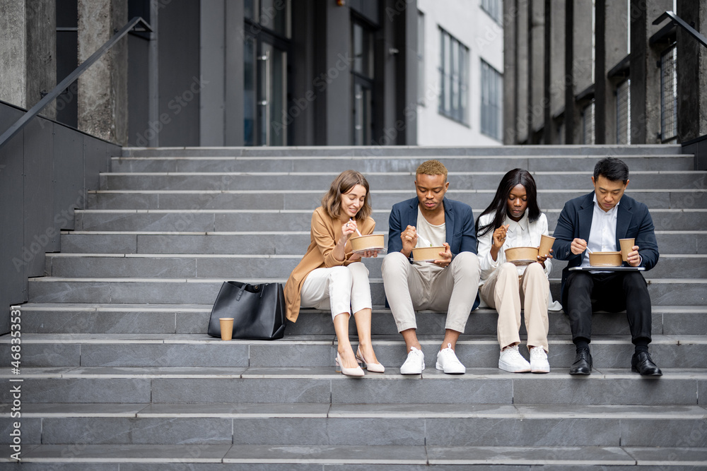 Multiracial business team talking, eating and drinking on stairs in city at daytime. Concept of rest