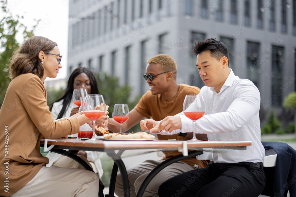 多种族商业团队在户外咖啡馆享用葡萄酒和披萨午餐。团队建设的概念