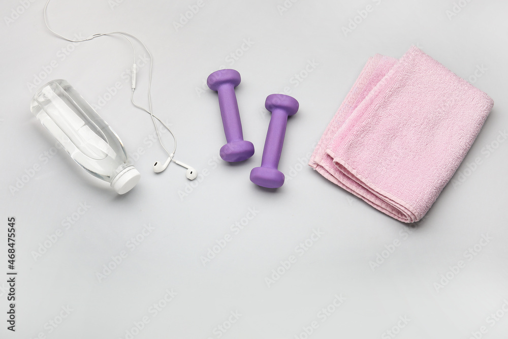 Dumbbells, earphones and bottle of water on light background