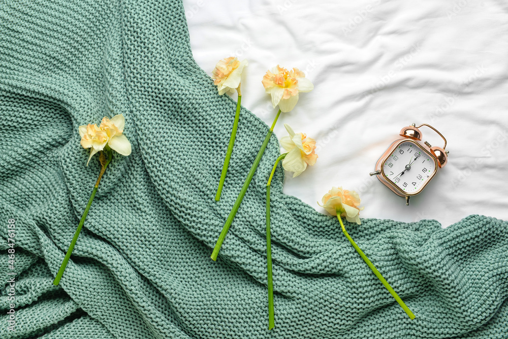 Narcissus flowers and alarm clock on crumpled fabric background