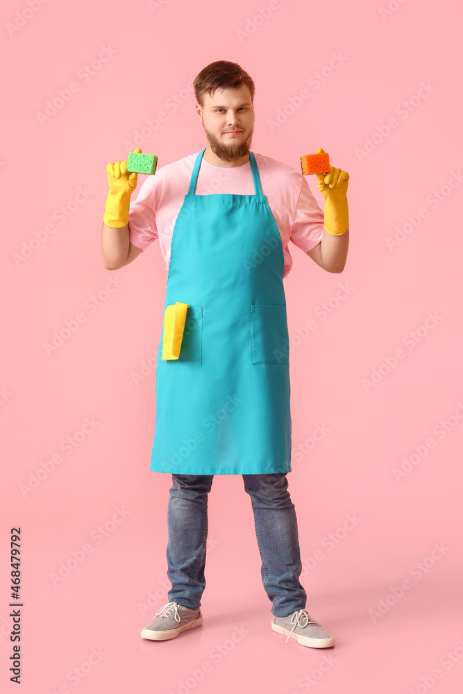 Young man with cleaning sponges on pink background