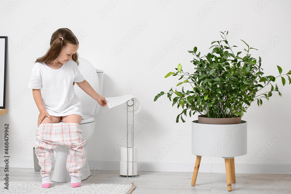 Little girl sitting on toilet bowl in bathroom