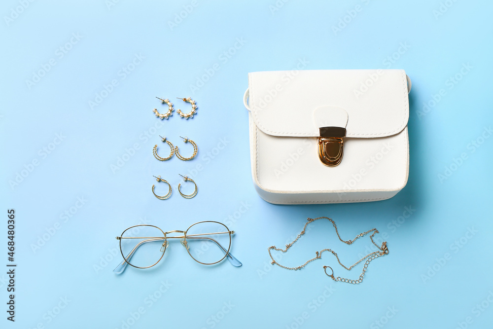 Composition with female handbag, glasses and stylish jewels on color background