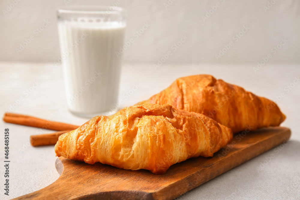 Wooden board with delicious croissants on white background