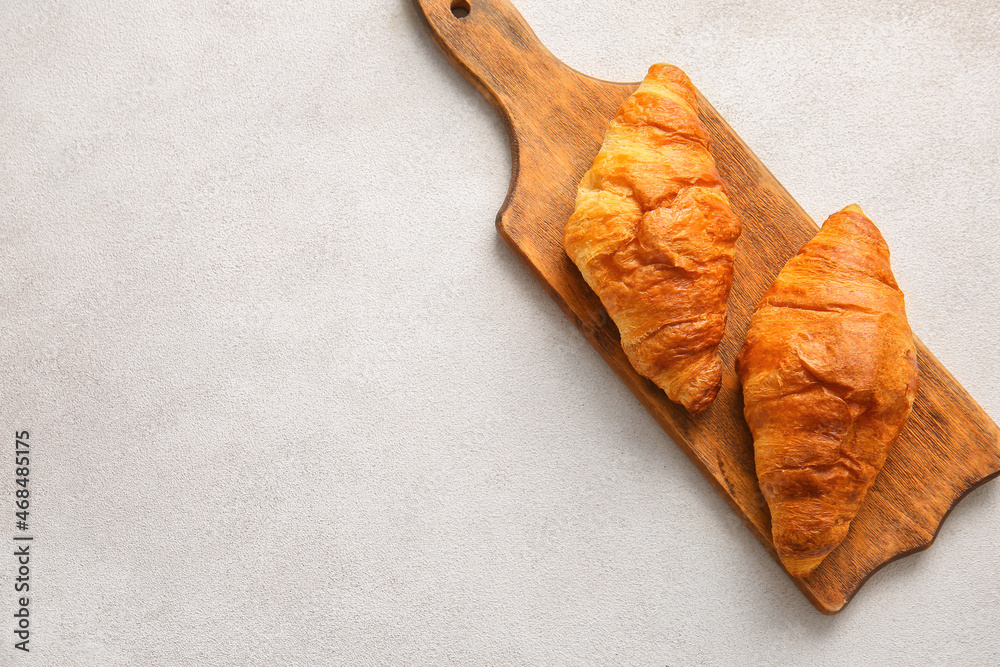 Wooden board with delicious croissants on white background