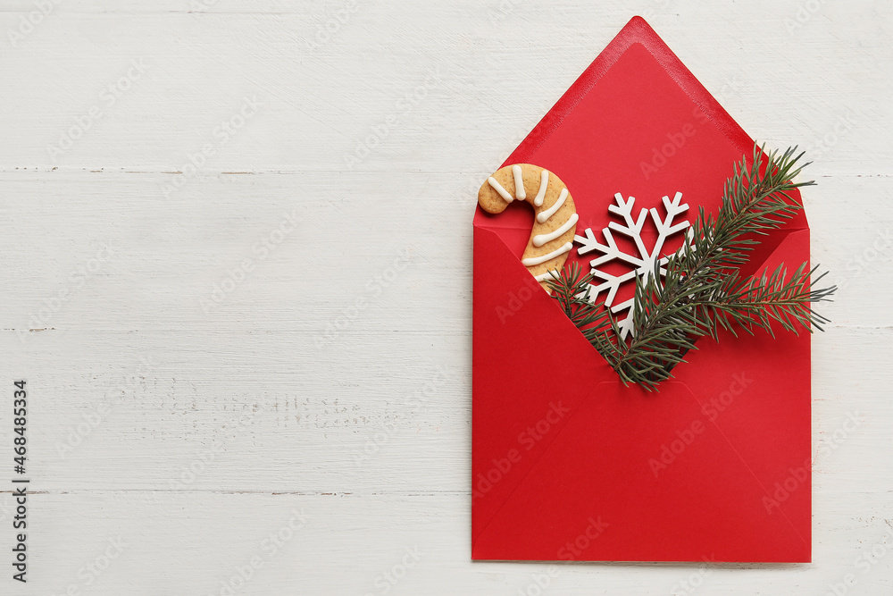 Envelope with Christmas cookie, snowflake and fir tree branch on white wooden background