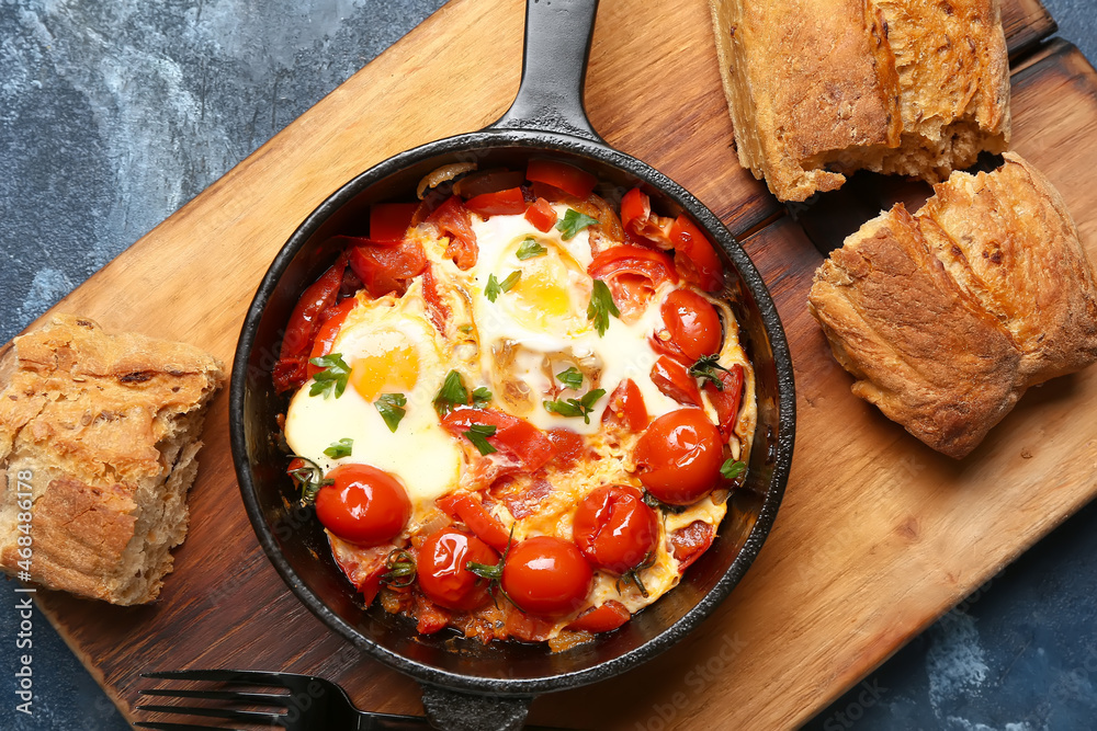 Frying pan with tasty Shakshouka and bread on blue background